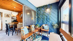 A cozy dining area with wooden chairs and a table, a kitchen with a coffee machine, and a blue wall with hanging vines. - Courchevel #5 2 Bedroom Condo by RedAwning (Mammoth Lakes)