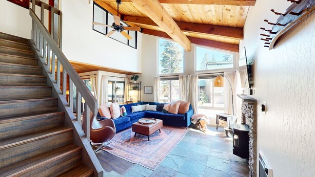 A spacious living room with a wooden staircase, a blue sectional sofa, a coffee table, and a fireplace. - Courchevel #5 2 Bedroom Condo by RedAwning (Mammoth Lakes)
