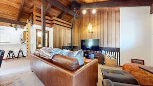 Un salon chaleureux avec un canapé en cuir, un téléviseur et un plafond en bois.