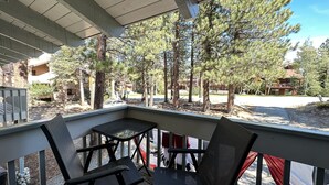 Un espace extérieur abrité, avec deux tables et des chaises, donnant sur une zone boisée avec des arbres et un bâtiment en arrière-plan.
