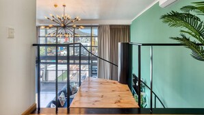 A wooden staircase with a metal railing, a hanging light fixture, and a view of a cityscape through large windows. - Always Power SOHO City Retreat Split level Apartment with Table Mountain View (Cape Town)