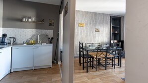 A modern kitchen with white cabinets, a dining area with a glass table and black chairs, and a wooden floor. - Résidence Kméléon (Le Mans)