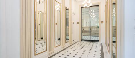 A hallway with mirrored walls, a tiled floor, and a chandelier.