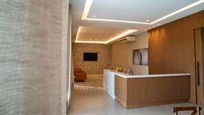Un área de recepción moderna con pared de piedra, televisor de pantalla plana, mostrador de recepción de madera y zona de estar con sillas de madera.