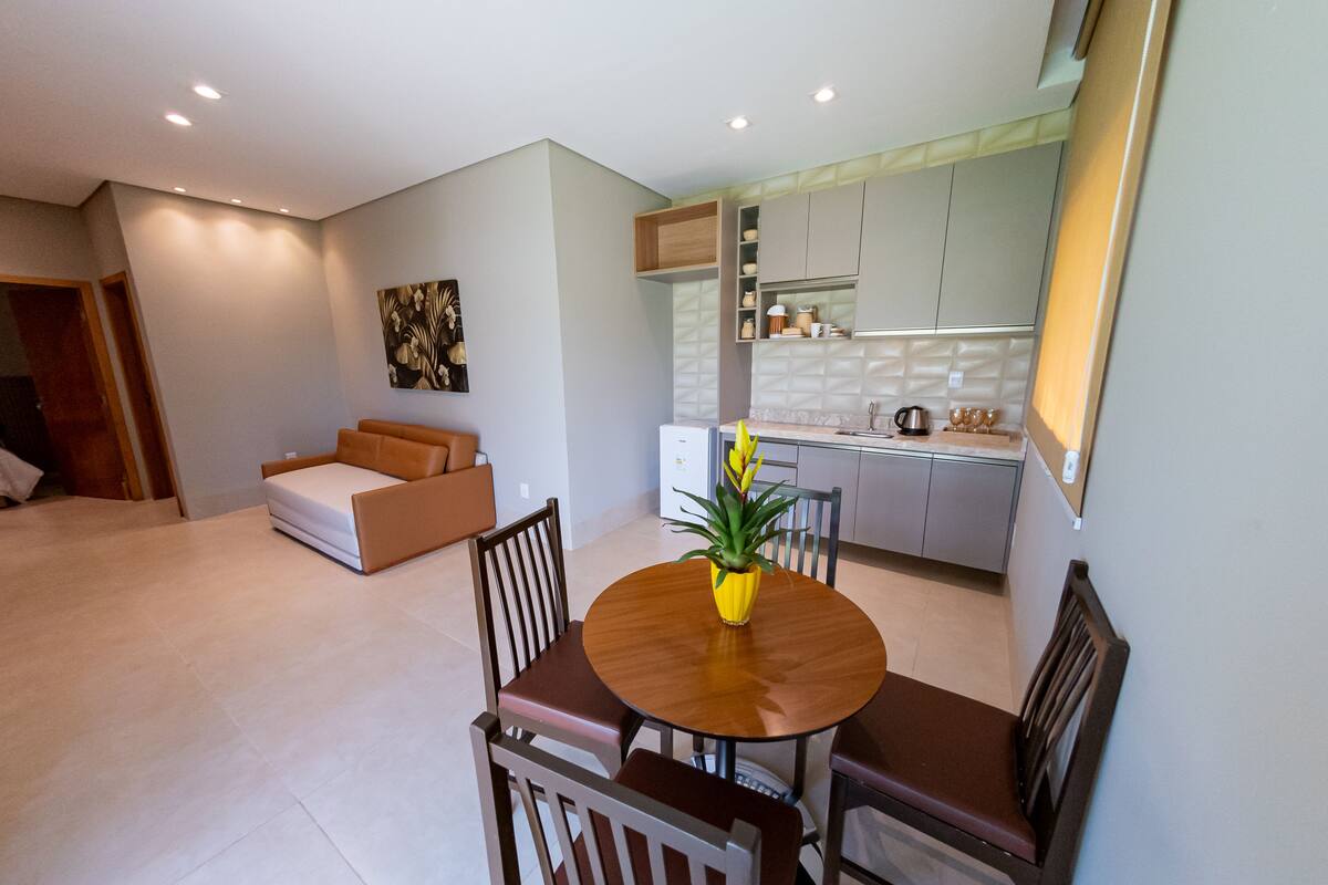 A modern living room with a dining table, chairs, a sofa, and a kitchen area with cabinets and appliances.