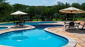 Una piscina con varias secciones, rodeada de baldosas de piedra y equipada con mobiliario y sombrillas.