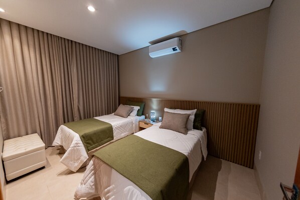 A hotel room with two beds, a bedside table, an air conditioning unit, and a window with blinds. - SPA AGUA MILAGROSA (Cuiabá)