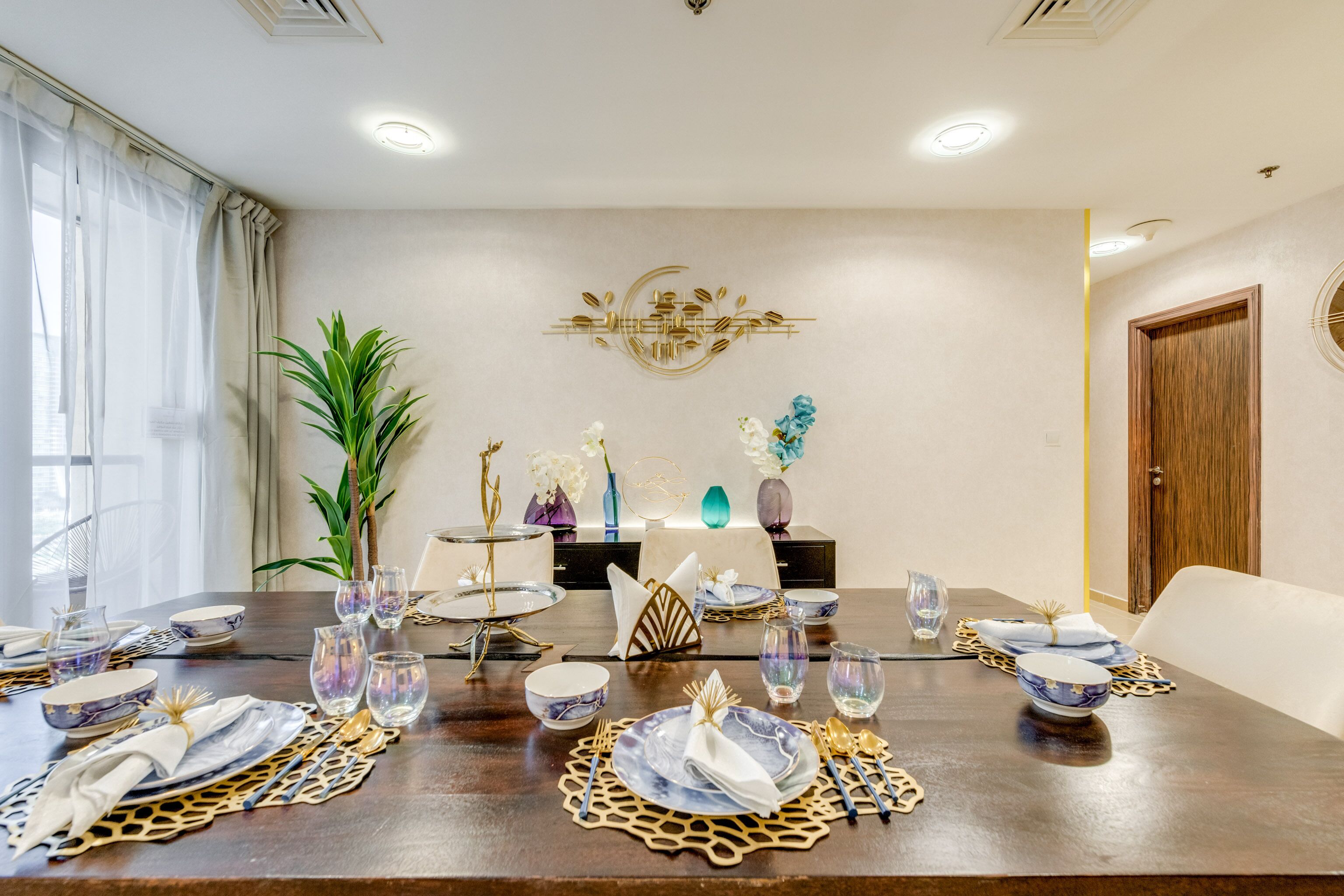 Ein Essbereich mit einem langen Tisch, der für eine Mahlzeit gedeckt ist, mit einem dekorativen Wandelement und einem Blumentopf.