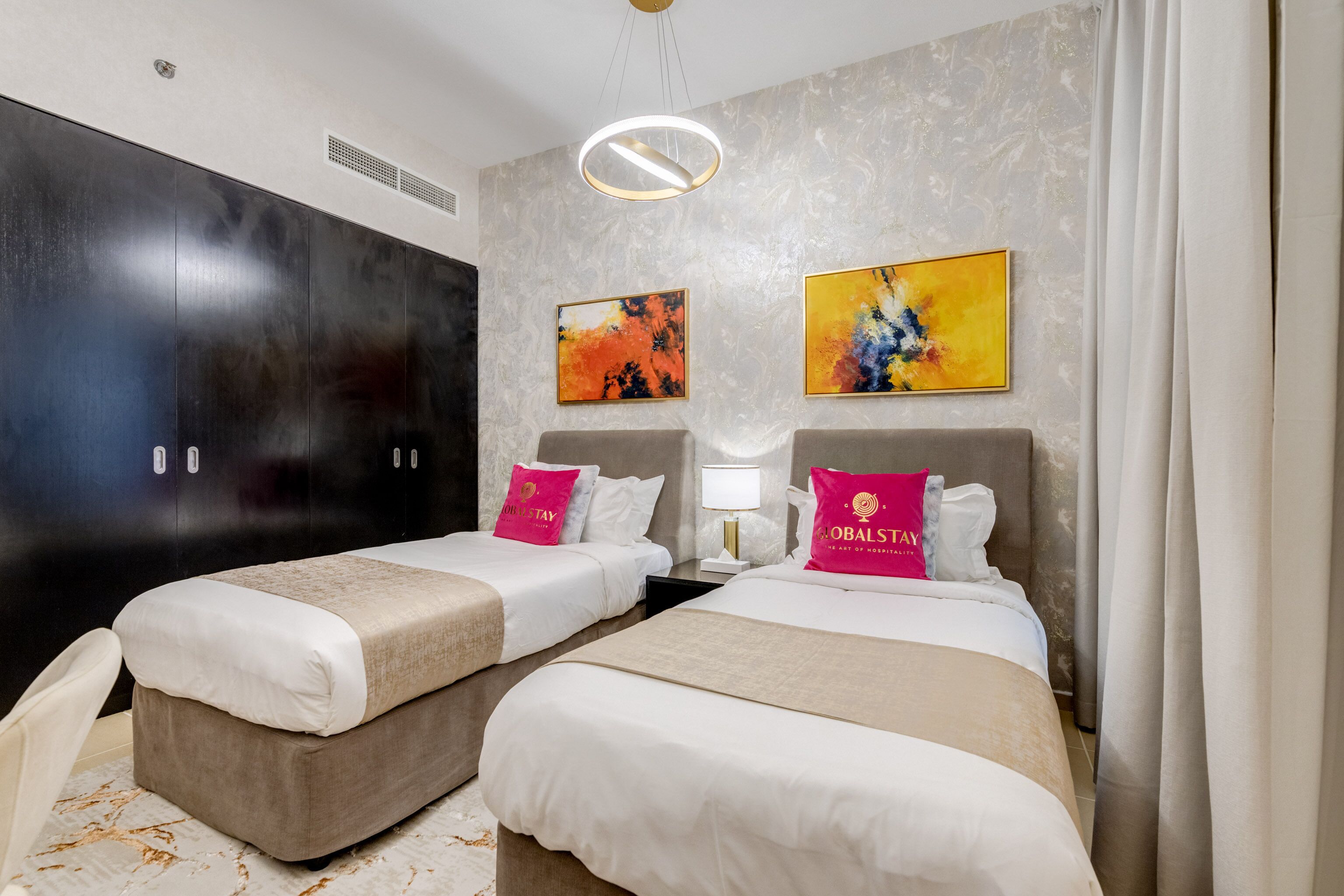 A hotel room with two beds, a large wardrobe, and two abstract paintings on the wall.