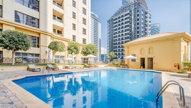 Una piscina con un perímetro de 1600 metros, rodeada de sillones de descanso y un pequeño edificio con techo de tejas.