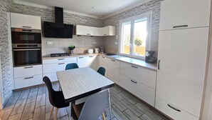 A modern kitchen with white cabinets, a built-in oven, a microwave, and a coffee maker. There is a window providing natural light and a view of the outdoors.