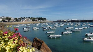 A marina with numerous boats docked, a sandy beach, and buildings in the background.