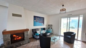 A living room with a stone fireplace, a sofa with blue cushions, a black armchair, and a large window with a view.