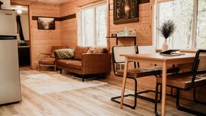 Un accogliente interno di una baita con arredamento in legno, un tavolo da pranzo con sedie, un divano e un frigorifero.