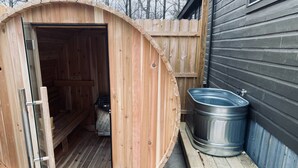 Una sauna in legno con porta scorrevole, una vasca idromassaggio in metallo e un pontile in legno.