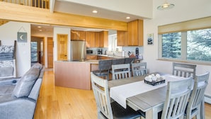 Amplia sala de estar con escalera de madera, cocina con alacenas de madera y comedor con mesa y sillas.
