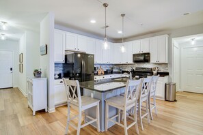 A modern kitchen with white cabinets, a central island with bar stools, stainless steel appliances, and pendant lighting.
