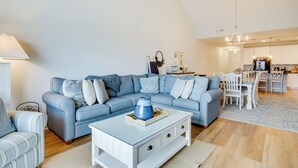 A living room with a blue sofa, a white coffee table, and a dining area with a white table and chairs. - Walk to Boardwalk! Ocean City Coastal Gem w/ Deck (Ocean City)