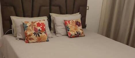A neatly made bed with a headboard, two pillows with floral patterns, and a plain bedspread.