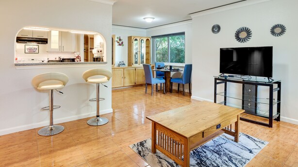 A modern kitchen with a built-in island, two bar stools, a dining area with a wooden table and chairs, and a TV on a glass stand. - Pet-friendly Houston Vacation Rental w/ Patio! (Houston)