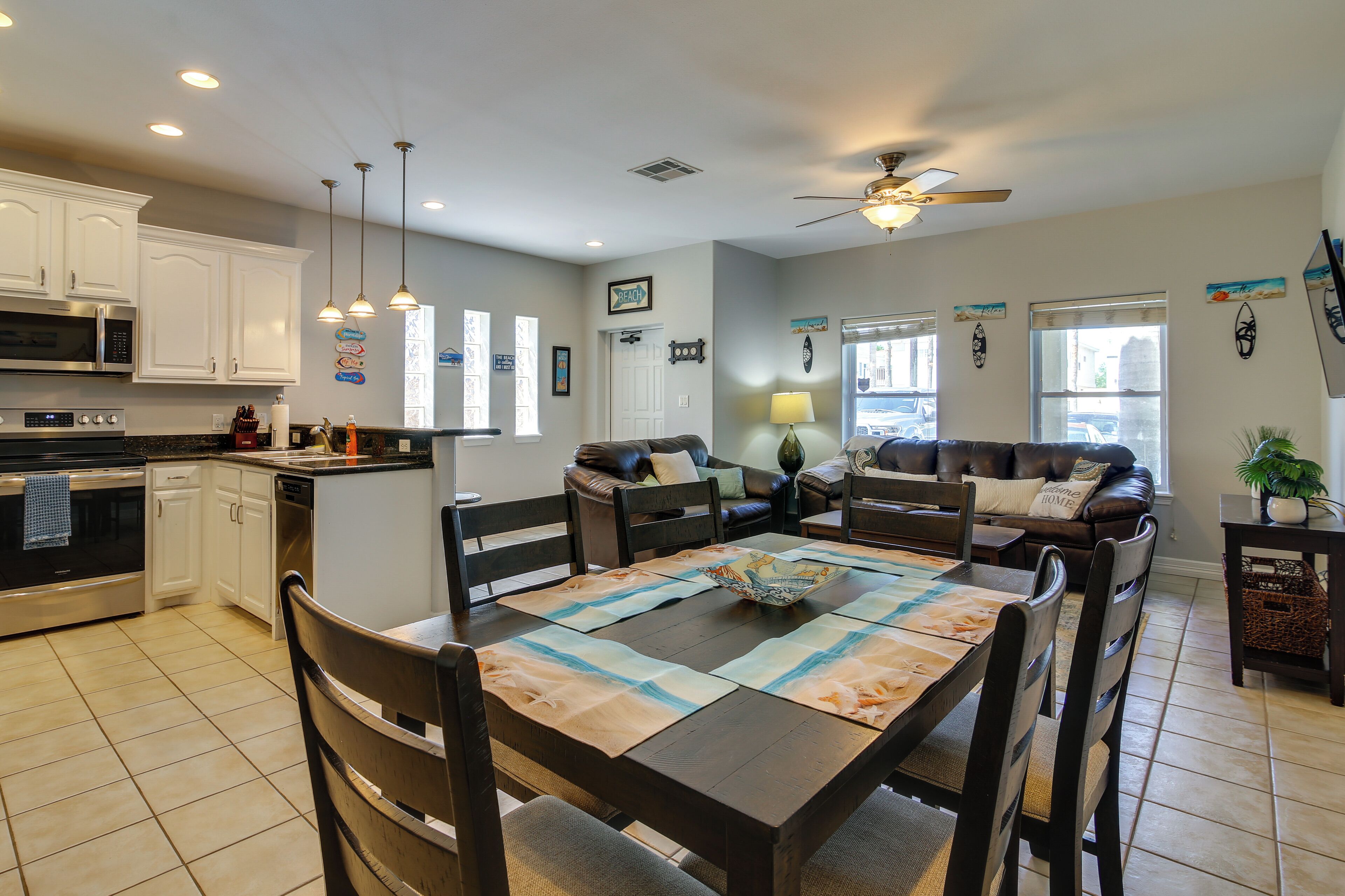 A modern kitchen with white cabinets, a dining area with a wooden table, and a living room with a brown leather couch.