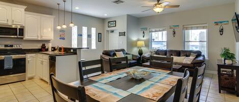 A modern kitchen with white cabinets, a dining area with a wooden table, and a living room with a brown leather couch.