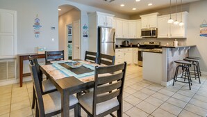 A modern kitchen with white cabinets, a stainless steel refrigerator, and a central island with bar stools. - South Padre Island Condo w/ Shared Outdoor Pool! (South Padre Island)