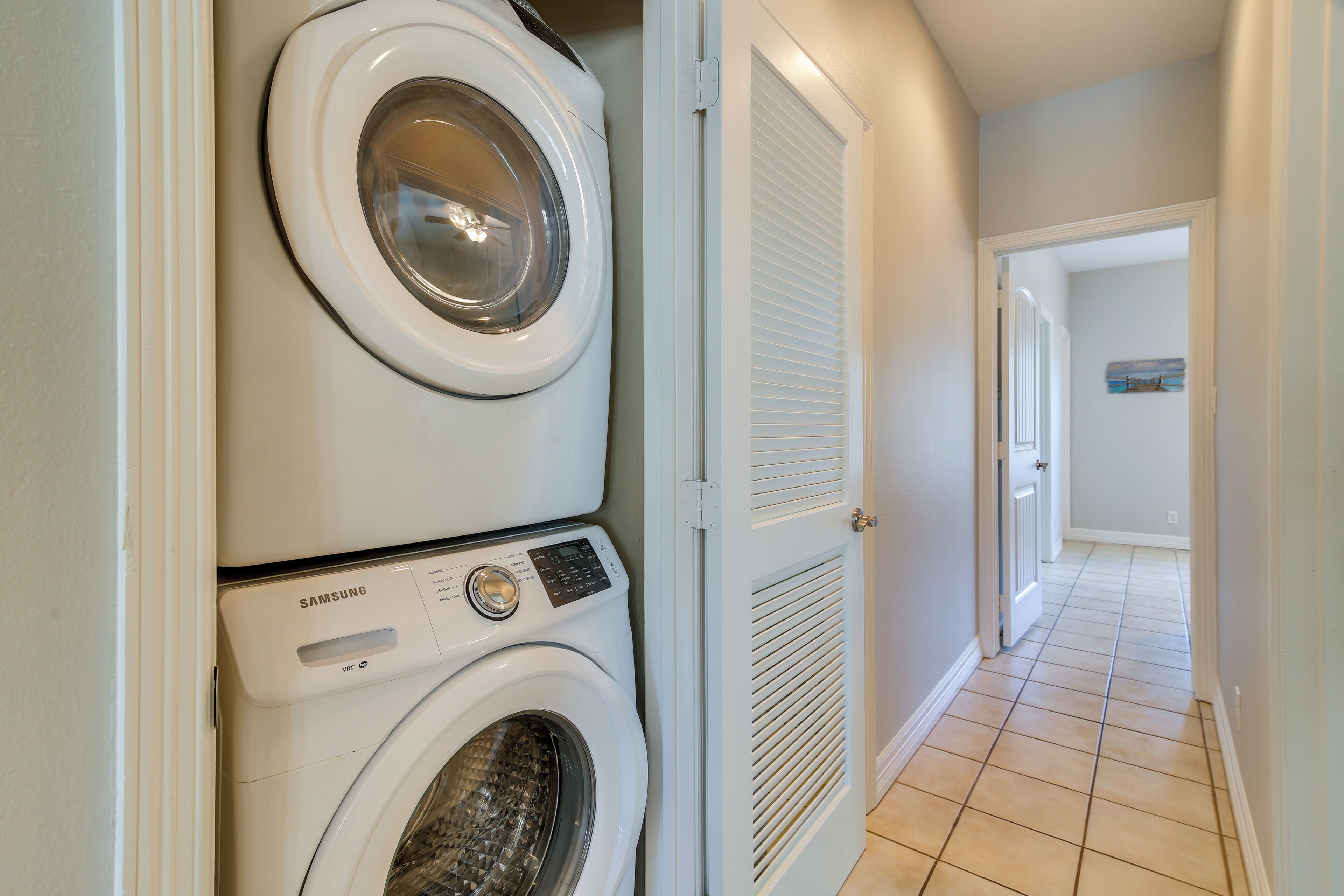 A laundry room with stacked washers and dryers, a door leading to another room, and a tiled floor.
