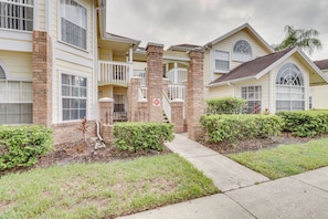 A multi-story residential building with a brick facade, multiple windows, and a small front yard with grass and shrubs. - 6 Mi to Disney: Family-friendly Condo in Kissimmee (Kissimmee)