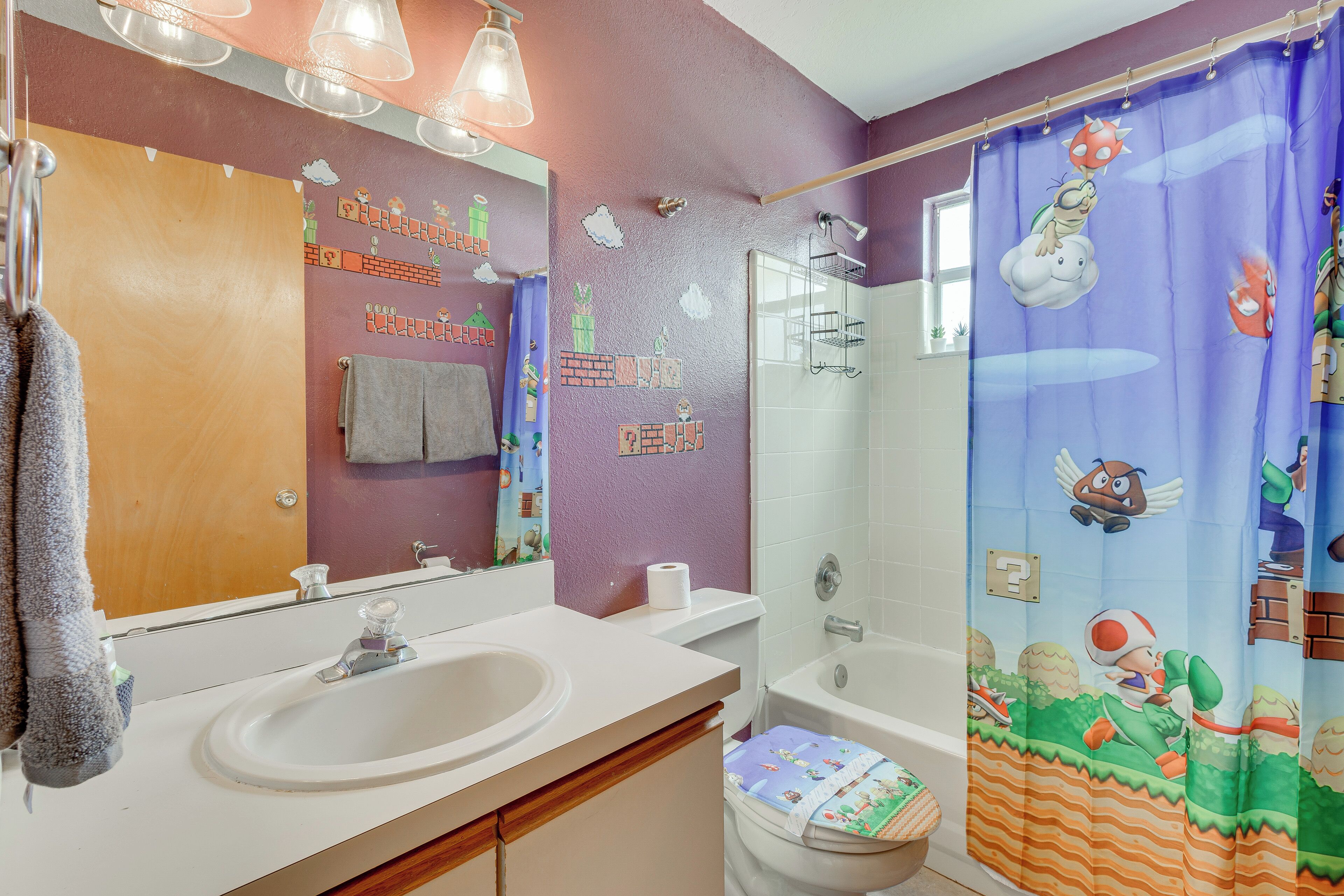 A bathroom with a sink, mirror, and shower curtain with a Mario theme.