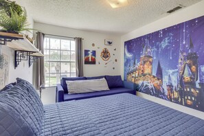 A bedroom with a large bed, a blue sofa, a window with curtains, and a wall with a castle-themed mural. - 6 Mi to Disney: Family-friendly Condo in Kissimmee (Kissimmee)