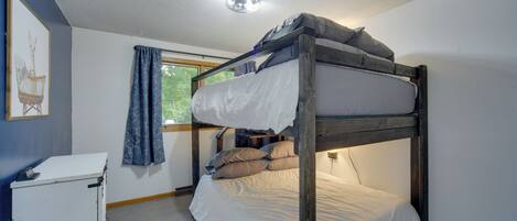 A bunk bed in a room with a small desk and a window with curtains.