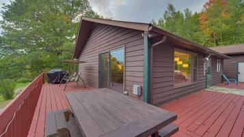 A wooden deck with a picnic table, a covered grill, and a glass door leading to a room.