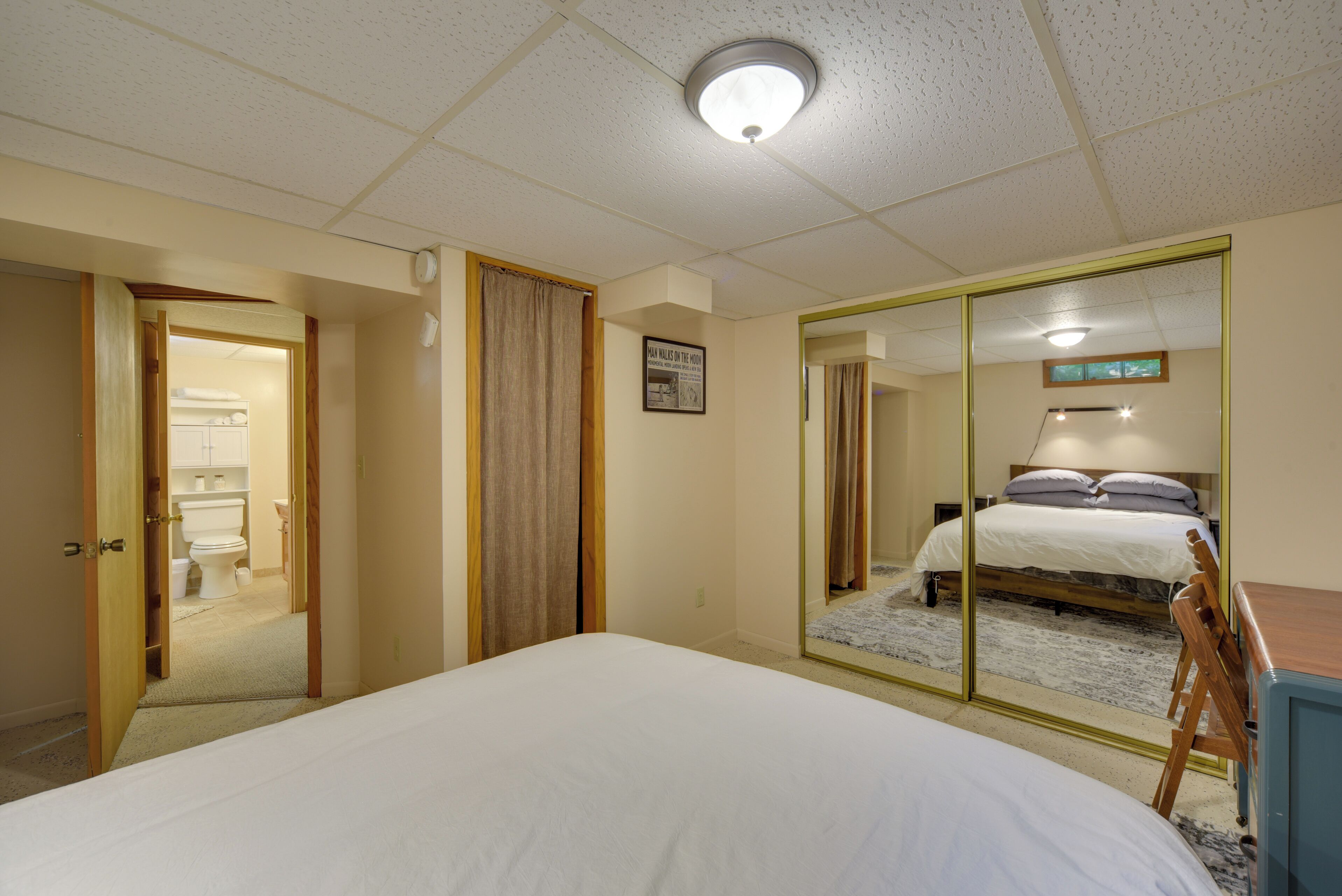 A bedroom with a bed, a mirror, a door leading to a bathroom, and a ceiling light.
