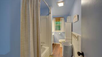 A bathroom with a bathtub, toilet, and a window with curtains.