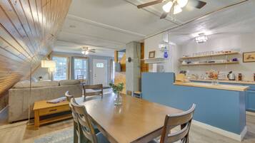 A dining area with a wooden table and chairs, a vase with flowers, and a kitchen area with blue cabinets and shelves.