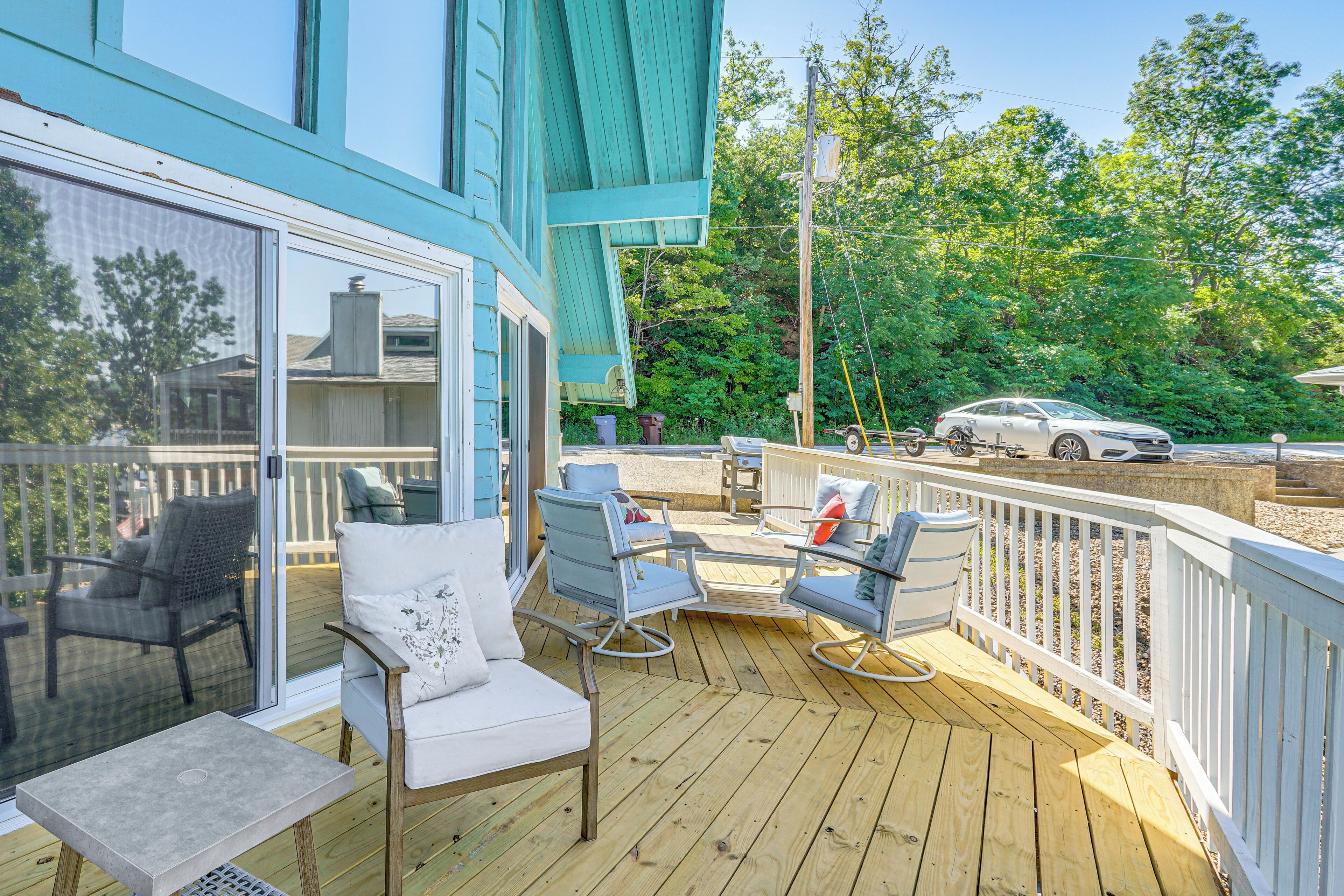 A wooden deck with outdoor furniture, a car parked nearby, and a view of a house in the background.