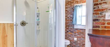 A bathroom with a glass shower enclosure, a white toilet, and a brick wall.