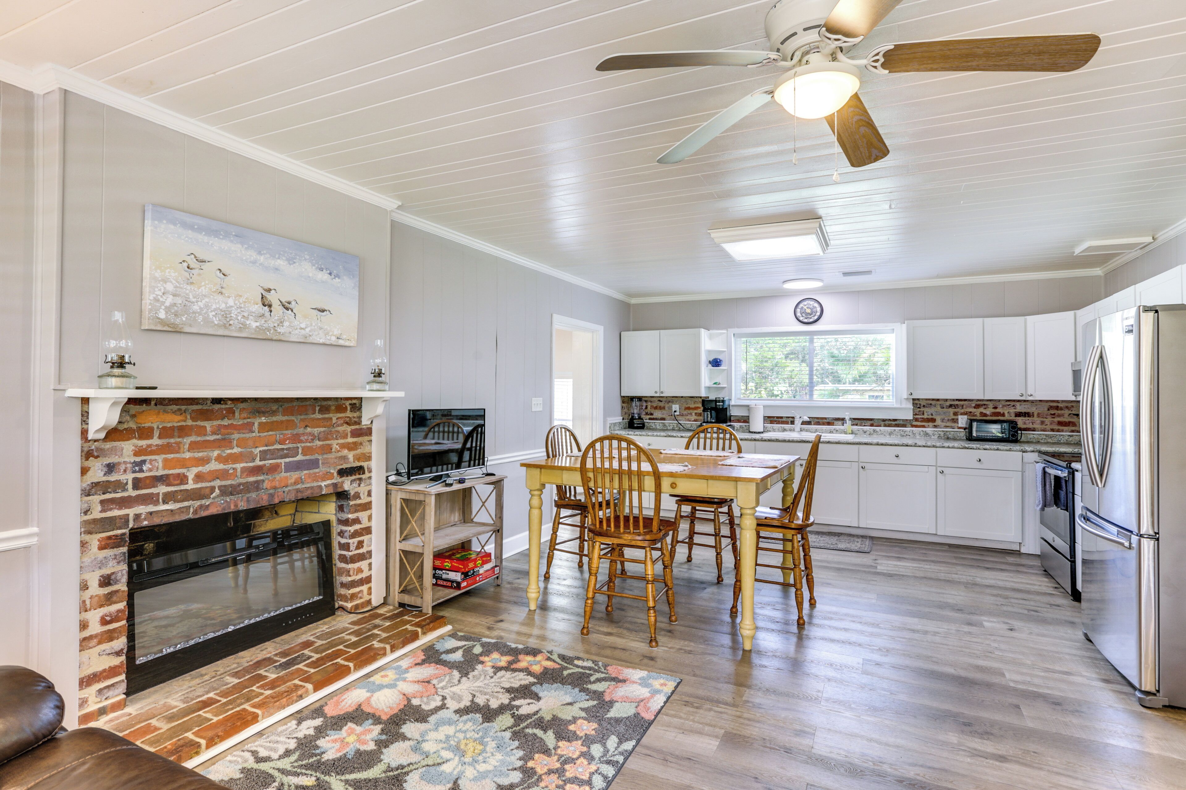 A spacious kitchen with white cabinets, a brick fireplace, and a dining area with wooden chairs.