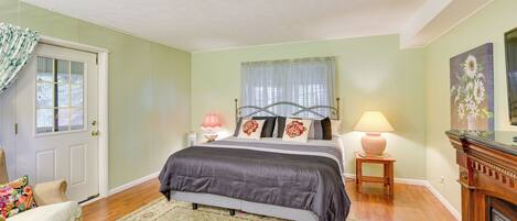 A bedroom with a bed, a nightstand, a lamp, a chair, a door, and a ceiling fan.