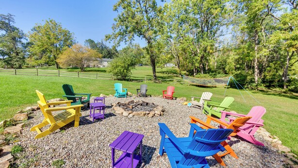 A fire pit area with colorful Adirondack chairs arranged around it, set on a gravel surface with trees in the background. - Jim Croces Farmhouse Apartment in Downingtown! (Downingtown)
