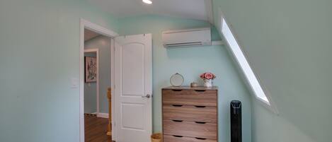 A bedroom with a bed, a dresser, a standing heater, and a door leading to another room.