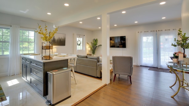 A spacious living area with a kitchen, a dining table, a sofa, and a TV mounted on the wall. - Fire Pit + On-site Pond: Hudson Valley Home! (Wappingers Falls)
