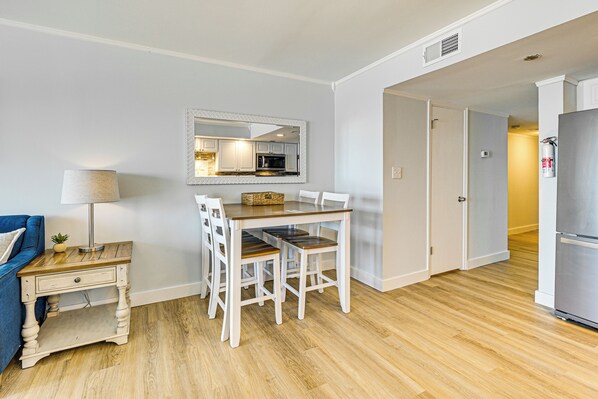 A dining area with a wooden table and white chairs, a small side table with a lamp, and a mirror above the table.