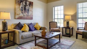 Een woonkamer met een bank, twee fauteuils, een salontafel, een schilderij en twee lampen.