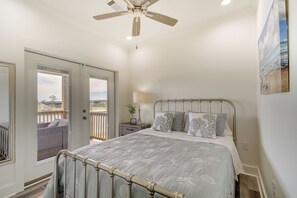 Un dormitorio con cama, ventilador de techo, mesita de noche, lámpara y vistas al exterior a través de una puerta corredera.