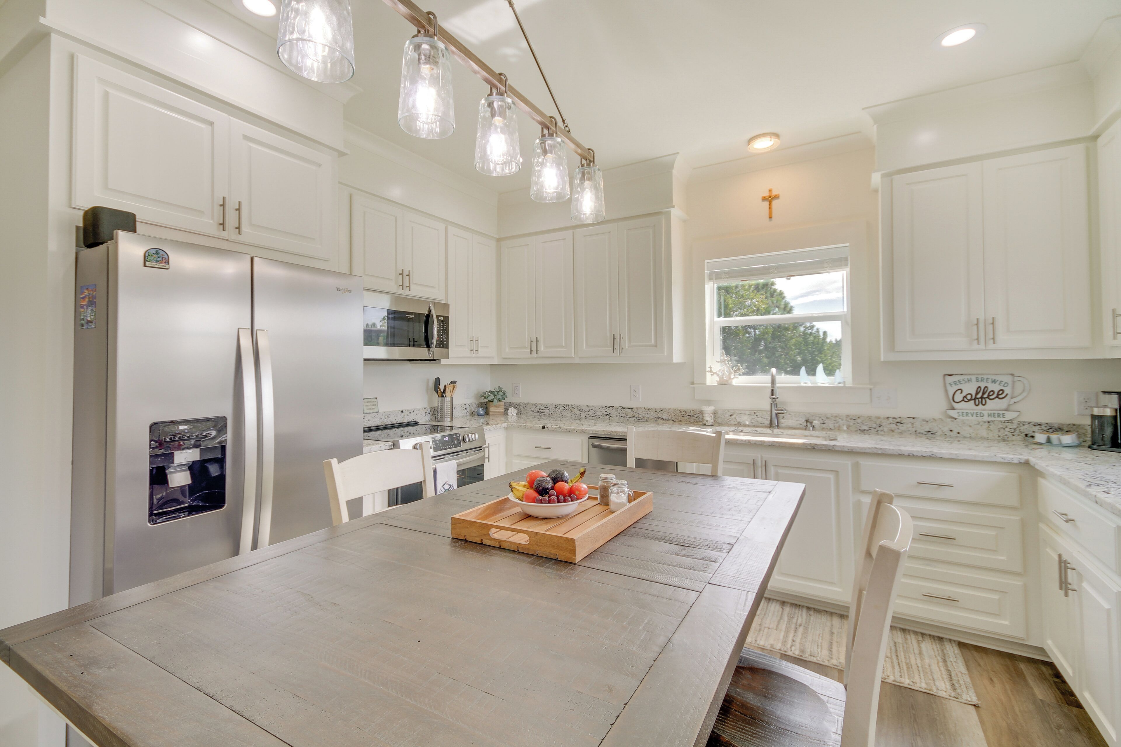 A modern kitchen with white cabinetry, a wooden dining table, and a fruit bowl.