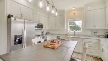 A modern kitchen with white cabinetry, a wooden dining table, and a fruit bowl.