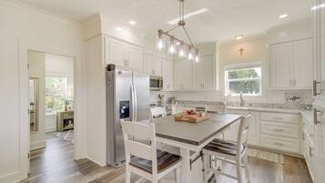 A kitchen with white cabinets, a wooden dining table, and a stainless steel refrigerator.