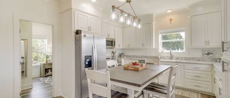 A kitchen with white cabinets, a wooden dining table, and a stainless steel refrigerator.